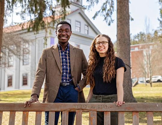 photo of two students standing behind a park bench